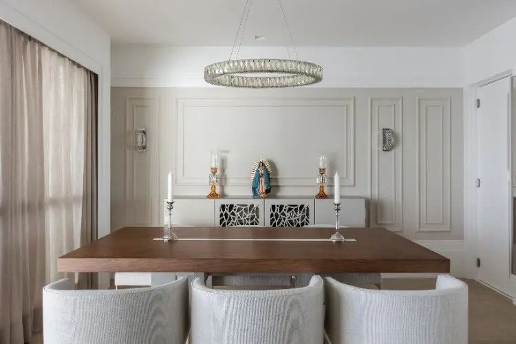Sala de jantar com mesa de madeira, poltronas cinzas, lustre, parede branca e bege com boiserie 