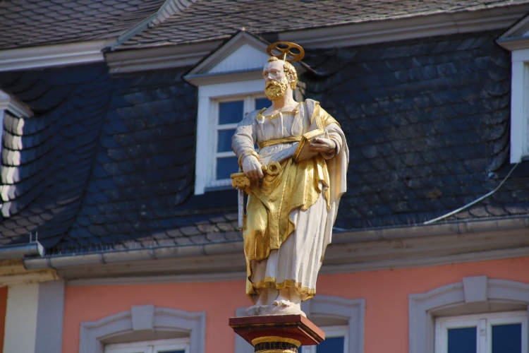 Estátua de São Pedro em branco e dourado, em frente a construção rosa
