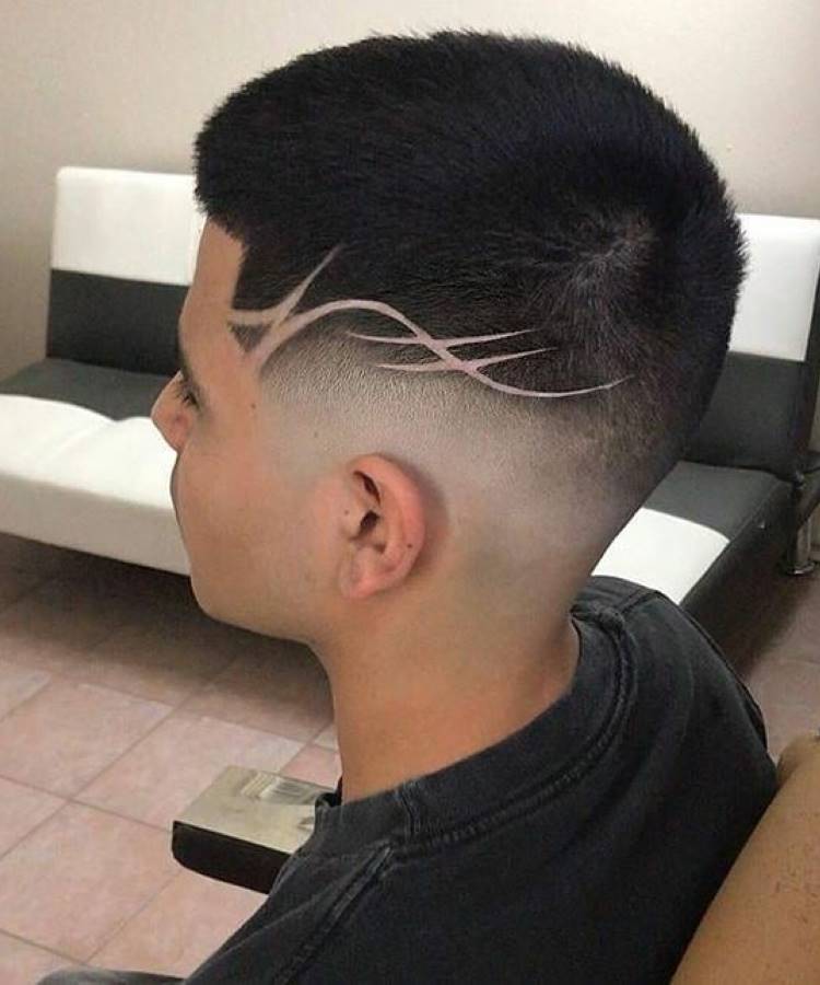 Um jovem de perfil com um **corte de cabelo buzz cut** e um degradê (fade) nas laterais e na nuca. O corte inclui um design de linhas curvadas raspadas que se estende do topo da cabeça até a nuca.