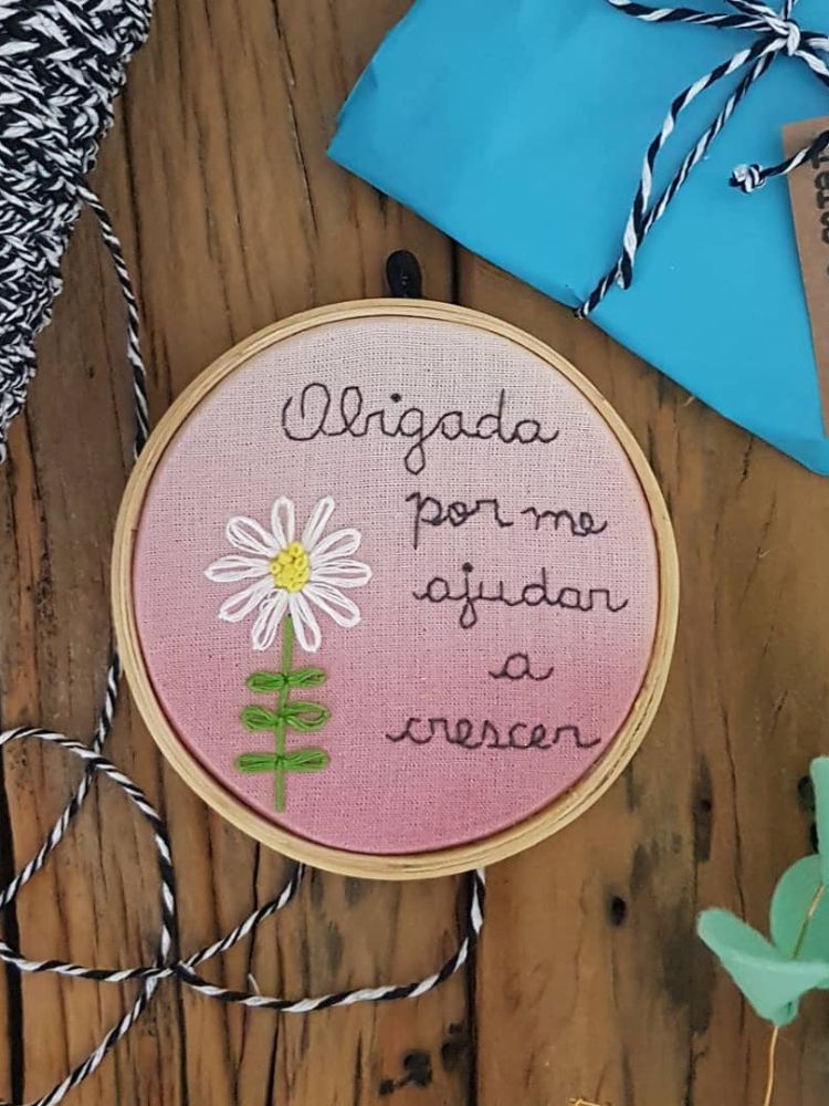 Bastidor rosa com bordado de margarida e frase "Obrigada por me ajudar a crescer"