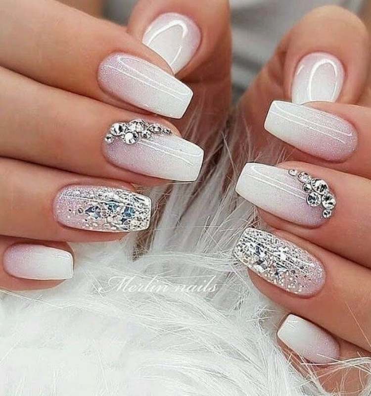 Unhas quadradas brancas com glitter, esmalte prata no anelar e pedrarias no médio