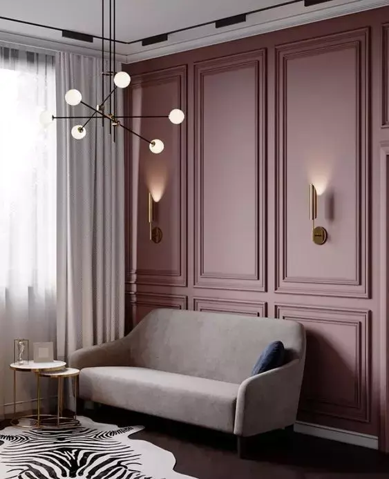 Sala de estar com parede vinho com boiserie, sofá bege escuro, duas mesas de centro em branco e dourado e lustre 