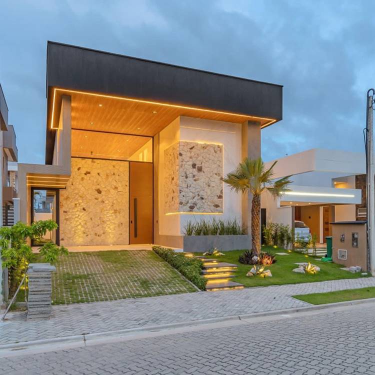 Fachada de casa moderna com iluminação quente, texturas em pedras e plantas em jardim
