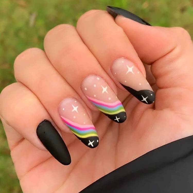 Mão com unhas arco-íris LGBTQIA+: Polegar: preto fosco Indicador: cor da unha com preto e estrelas Médio: cor da unha com arco-íris e preto com estrelas Anelar: cor da unha com arco-íris e preto com estrelas Mínimo preto fosco