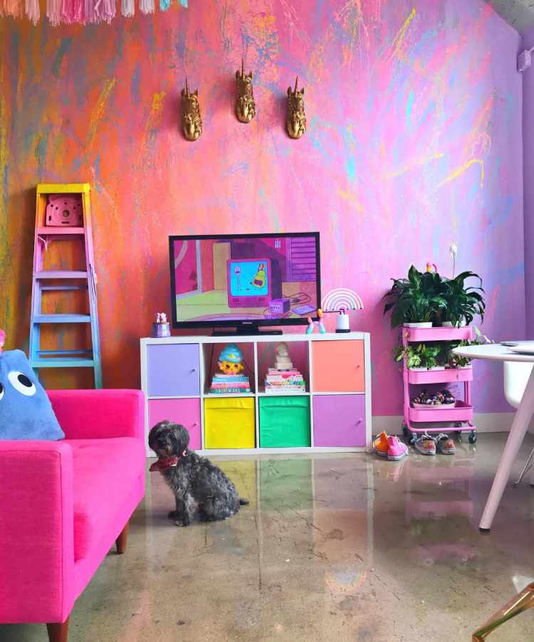 Sala com parede colorida, móvel da televisão colorido, aparador rosa com planta, escada colorida, poltrona rosa e mais