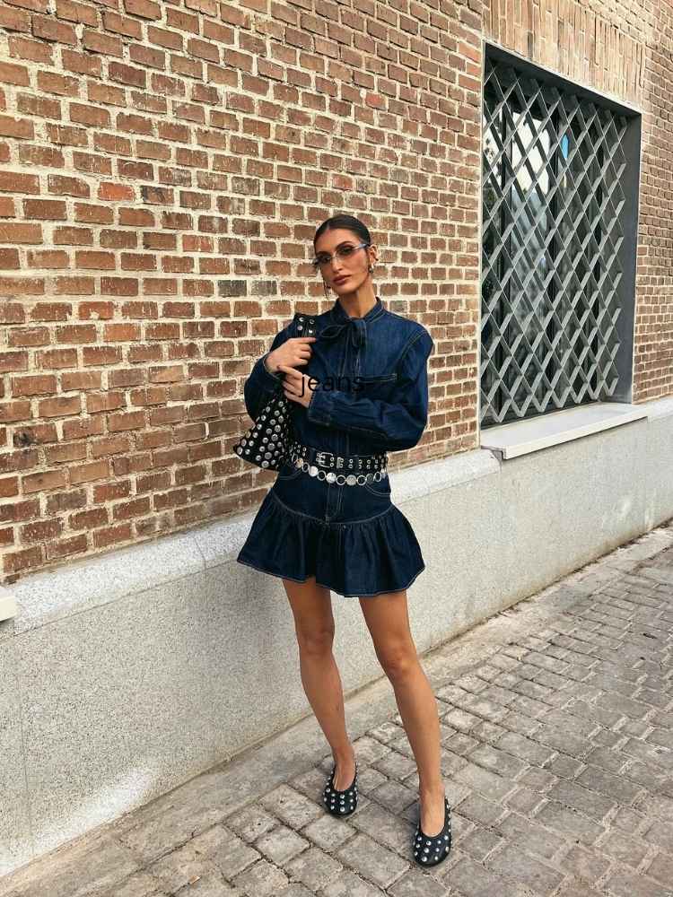 Mulher de pele clara de camisa e minissaia jeans, além de cintos
