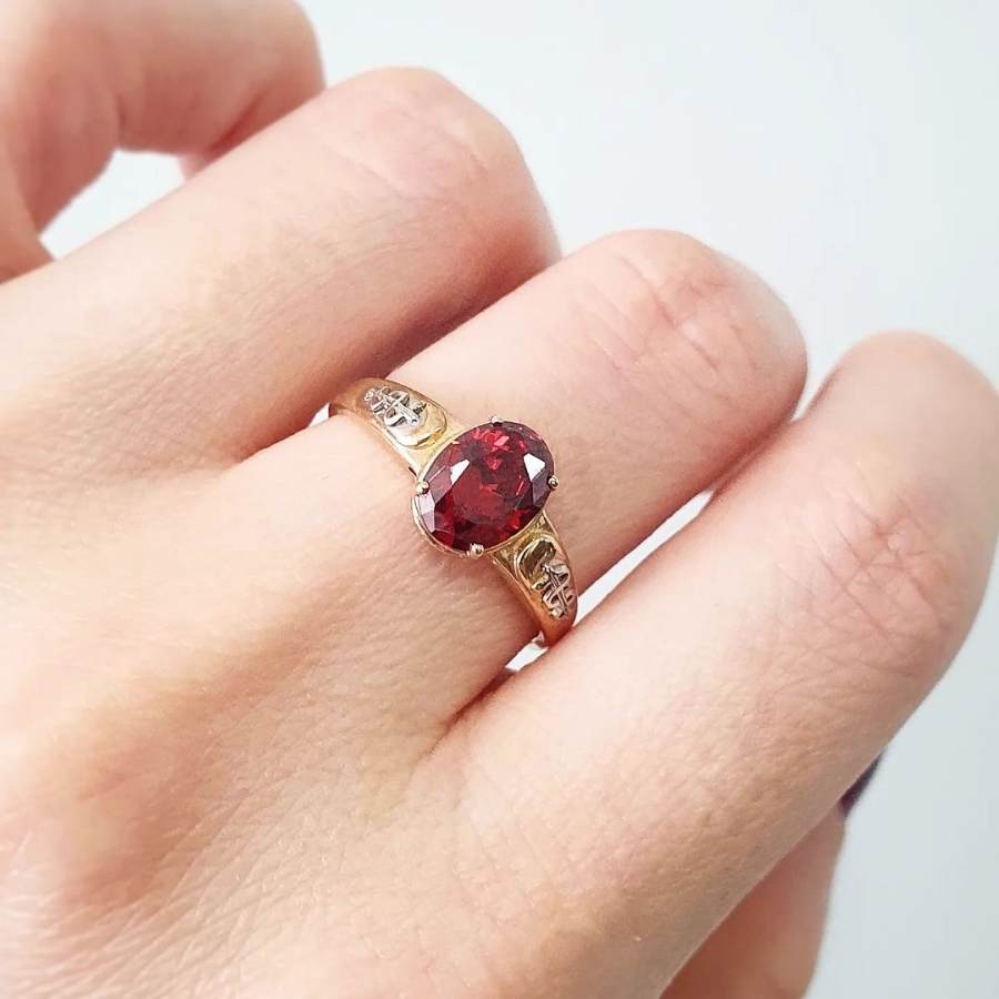Mulher de pele clara usando anel dourado com pedra vermelha no dedo médio