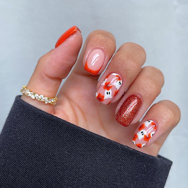 Mão com unhas médias quadradas decoradas para o Halloween nas cores branco, preto laranja e glitter laranja com fantasminhas e flores