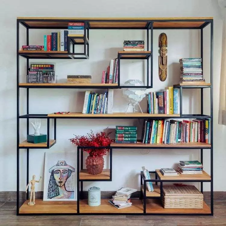 Estante quadrada de metal e madeira, com nichos vazados. Nela, há quadros, livros, vaso de planta e outros itens decorativos. 