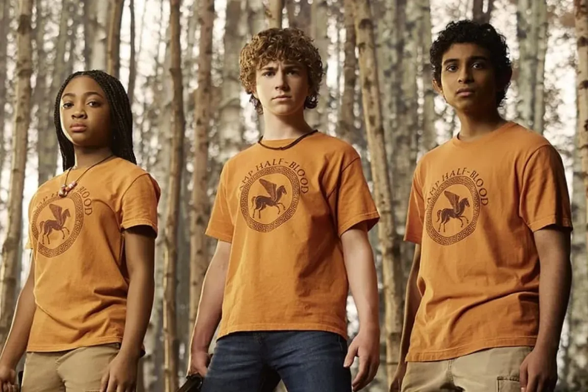 Três jovens usando camisetas do Acampamento Meio-Sangue em cena da série Percy Jackson