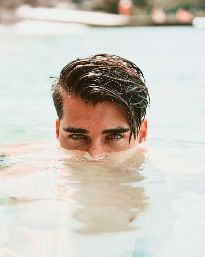 Homem de pele clara e olhos verdes com parte do rosto submersa no mar 
