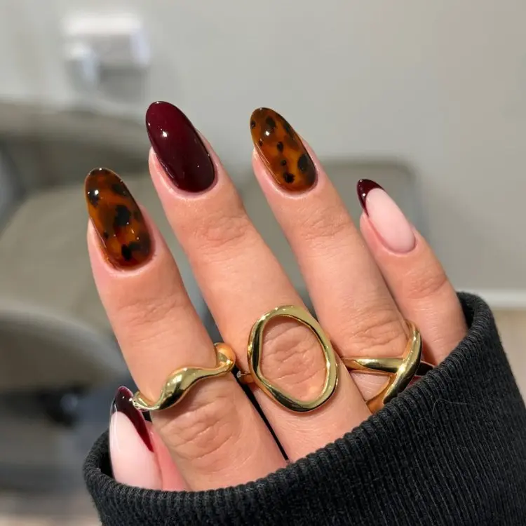 Mão de pele clara com anéis dourados e unha almond em animal print onça, vinho e nude 