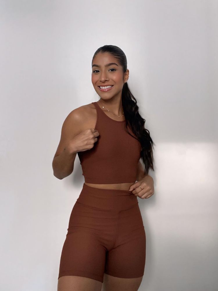 Mulher de pele morena usando conjunto fitness marrom, de cropped e shorts
