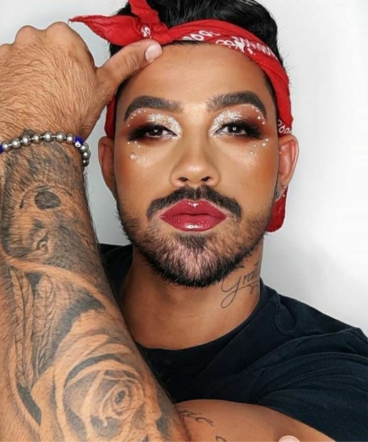Selfie de homem de pele morena com bandana vermelha e maquiagem vermelha iluminada e com strass