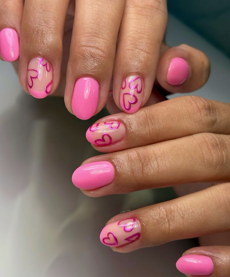 Unhas pintadas de rosa vibrante com detalhes de corações desenhados em linhas rosa escuro sobre base transparente. As mãos estão bem cuidadas, com pele suavemente iluminada. Fundo desfocado em tons neutros, destacando o design delicado e romântico das unhas.