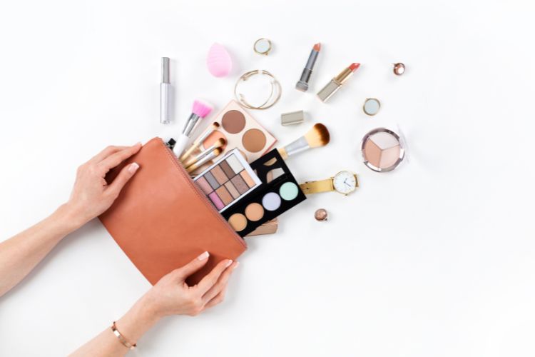 Mãos de mulher segurando nécessaire de couro com itens de maquiagem: pincéis, sombra, contorno, blush e batom