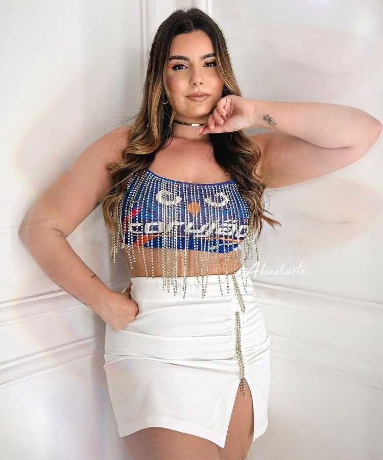 Mulher de pele clara com abadá azul customizado com franja de strass e saia branca com fenda