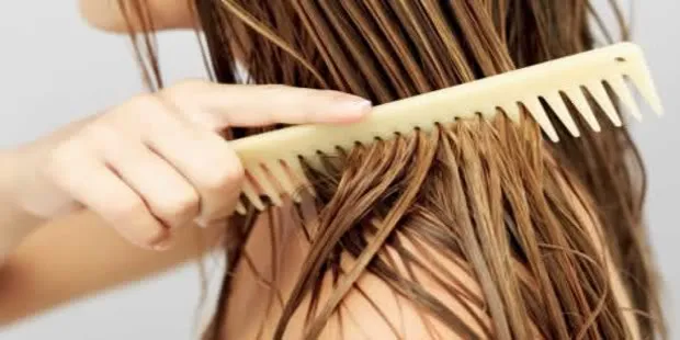 Mulher penteando o cabelo com pente de madeira para evitar queda de cabelo.