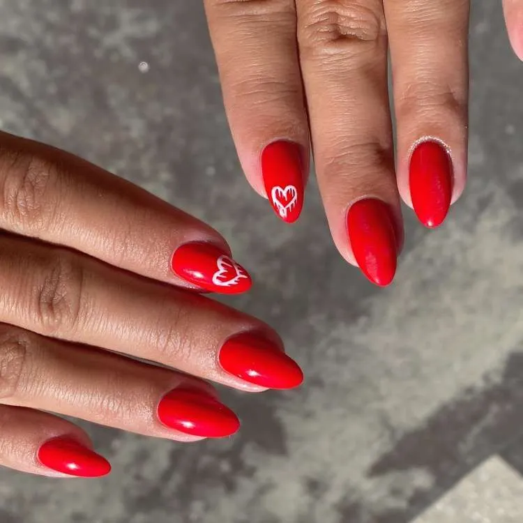 Unhas vermelhas decoradas, coração branco no dedo indicador