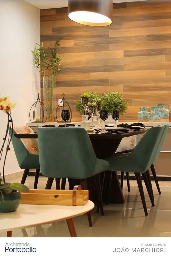 Sala de jantar com parede branca, parede de madeira, mesa marrom com cadeiras verdes e mesa posta