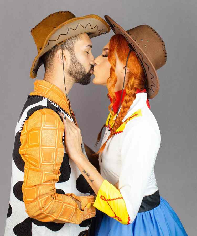 Traje de Dia das Bruxas para namorados: Jessie e Woody. Ele com camisa laranja e estampa de vaca, enquanto ela usa camisa branca com detalhe em amarelo e lenço vermelho. ambos de chapéu de cowboy