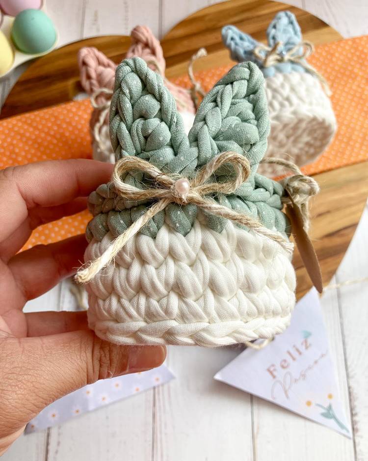 Uma mão segura uma cestinha de amigurumi com uma cordinha em formato de laço.


