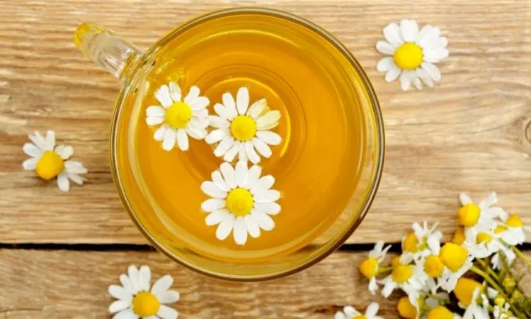 Xícara de vidro com chá de camomila e flores.