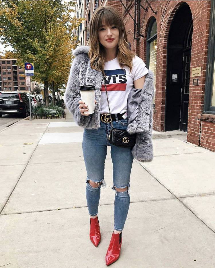 Mulher de pele clara usando camiseta branca e Levi's, casaco de pele, calça jeans skinny destroyed e bota vermelha