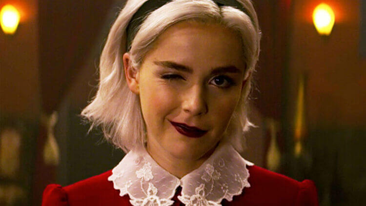 imagem da série Mundo sombrio de Sabrina foto da personagem principal de O Mundo Sombrio de Sabrina. Ela usa tiara preta, vestido vermelho com gola branca e está piscando um olho