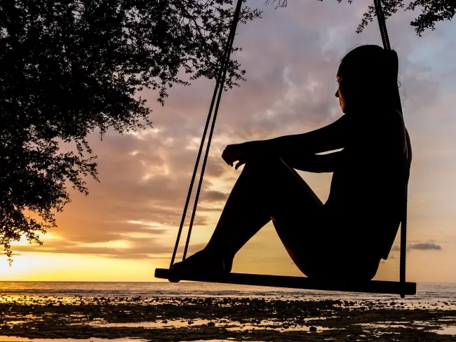 Frase para foto pensativa mulher sentada no balanço assiste ao pôr do sol na praia