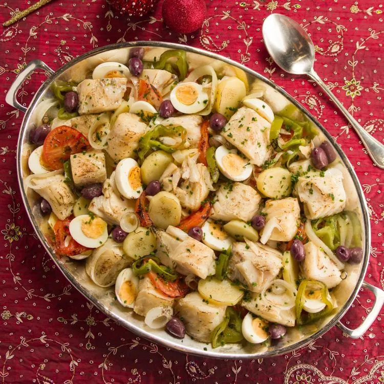 Um refratário contendo uma bacalhoada com legumes, batatas e ovos. Em cima de uma mesa com uma toalha de Natal