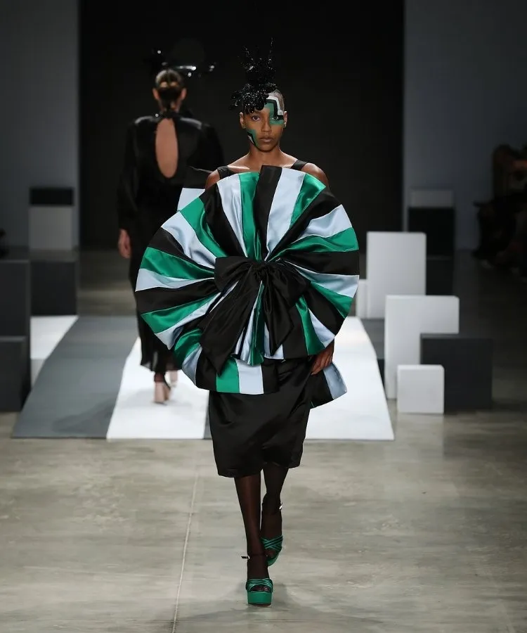 Foto de modelo na passarela usando vestido preto com roseta listrada em azul claro e verde