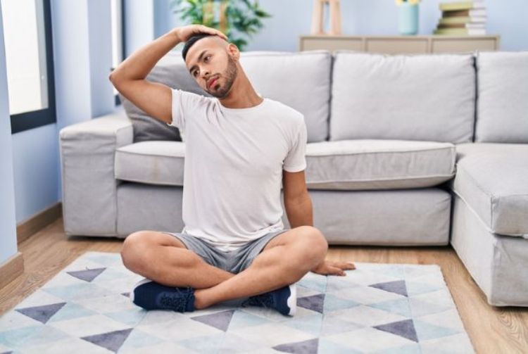 homem alongando pescoço enquanto está sentado no chão. Camiseta branca e shorts preto