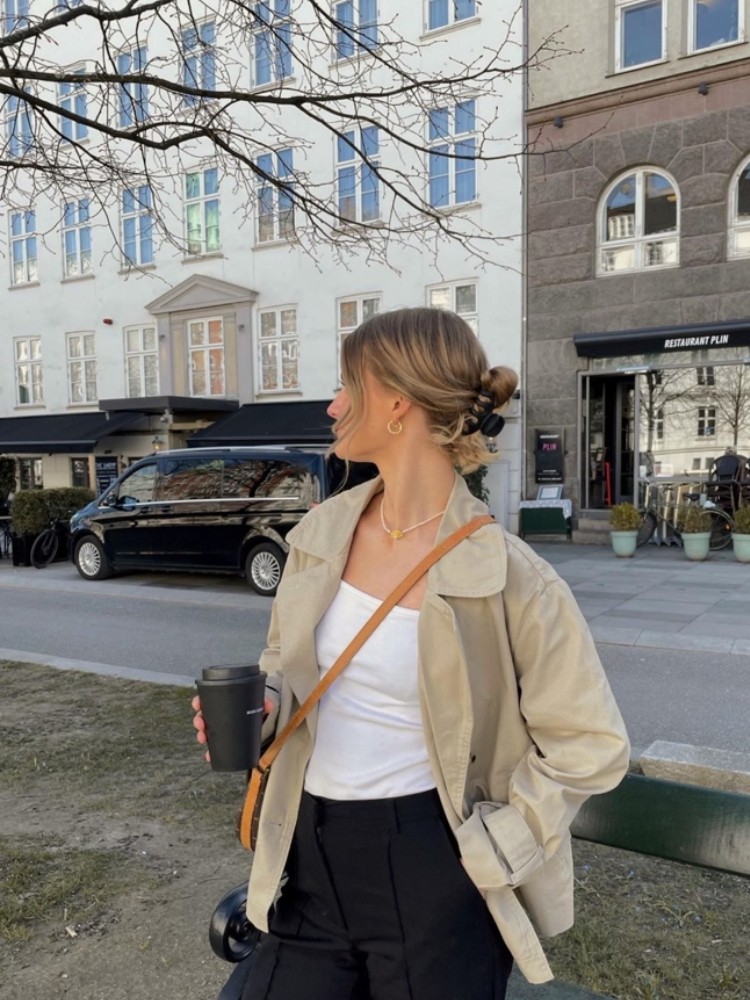 mulher usando regata branca com calça de alfaiataria preta com sobreposição de uma jaqueta bege e bolsa marrom transversal