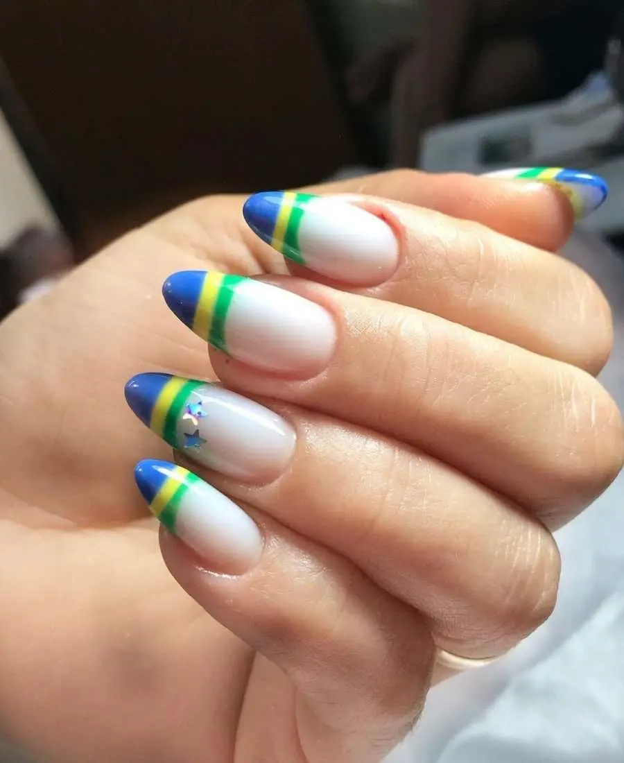 Imagem de mão decoradas com esmalte. Cores usadas: verde, azul, amarelo. Além de estrelas decorativas. Arte, francesinha com as cores da bandeira + estrelas no dedo anelar.