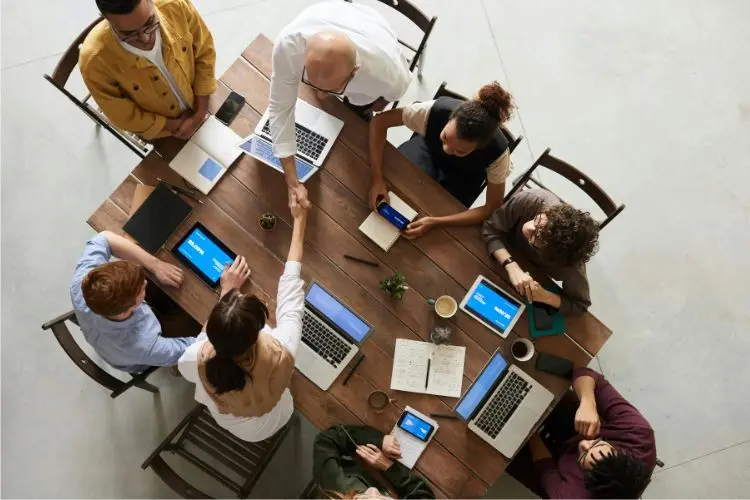 Foto de mesa de trabalho vista de cima, com dois colegas dando aperto de mãos