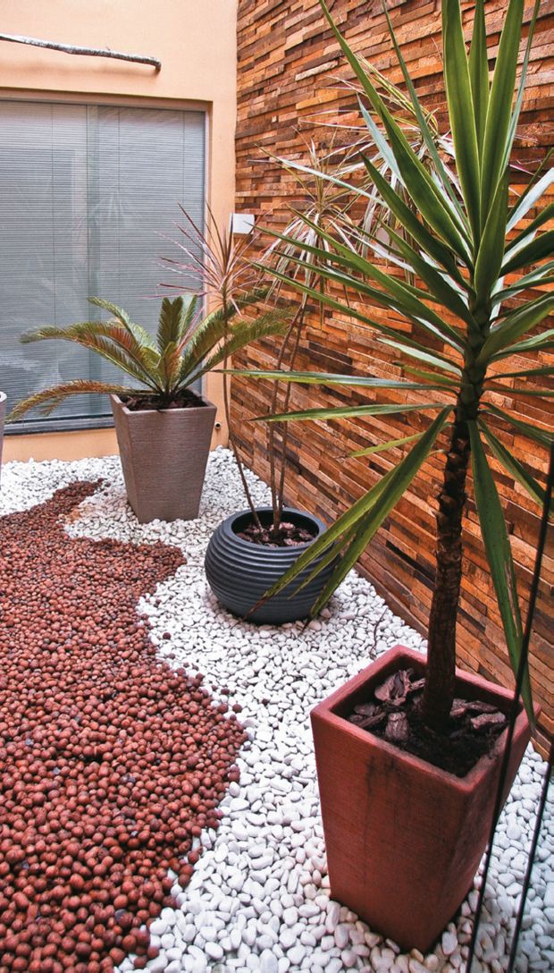 Jardim de inverno com pedras brancas e marrons, parede marrom e 3 vasos 