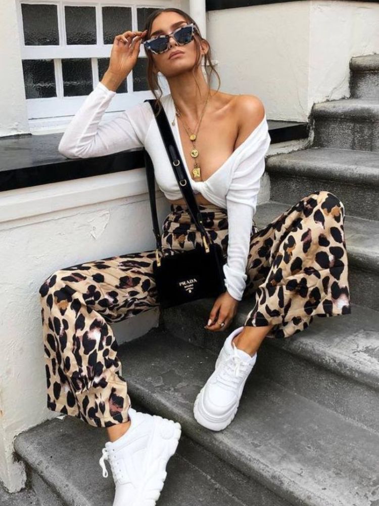 Mulher de pele clara usando cropped branco com calça de onça