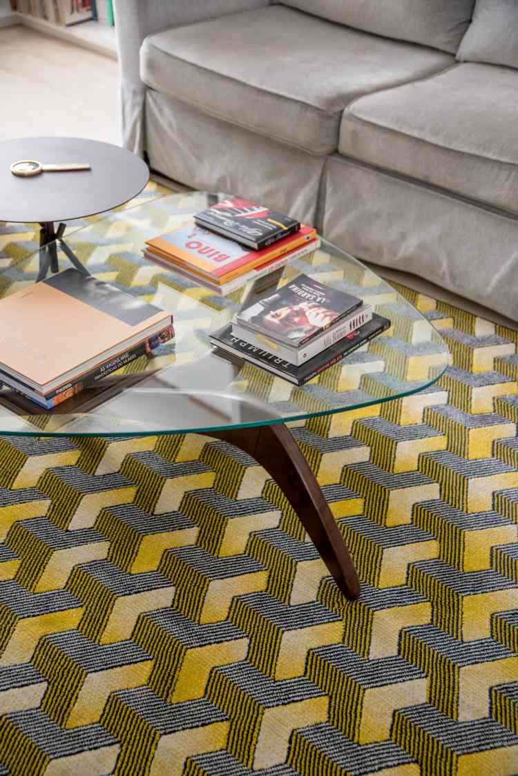 mesa de centro de sala de estar de vidro triangular, livros em cima e tapete estampado em baixo