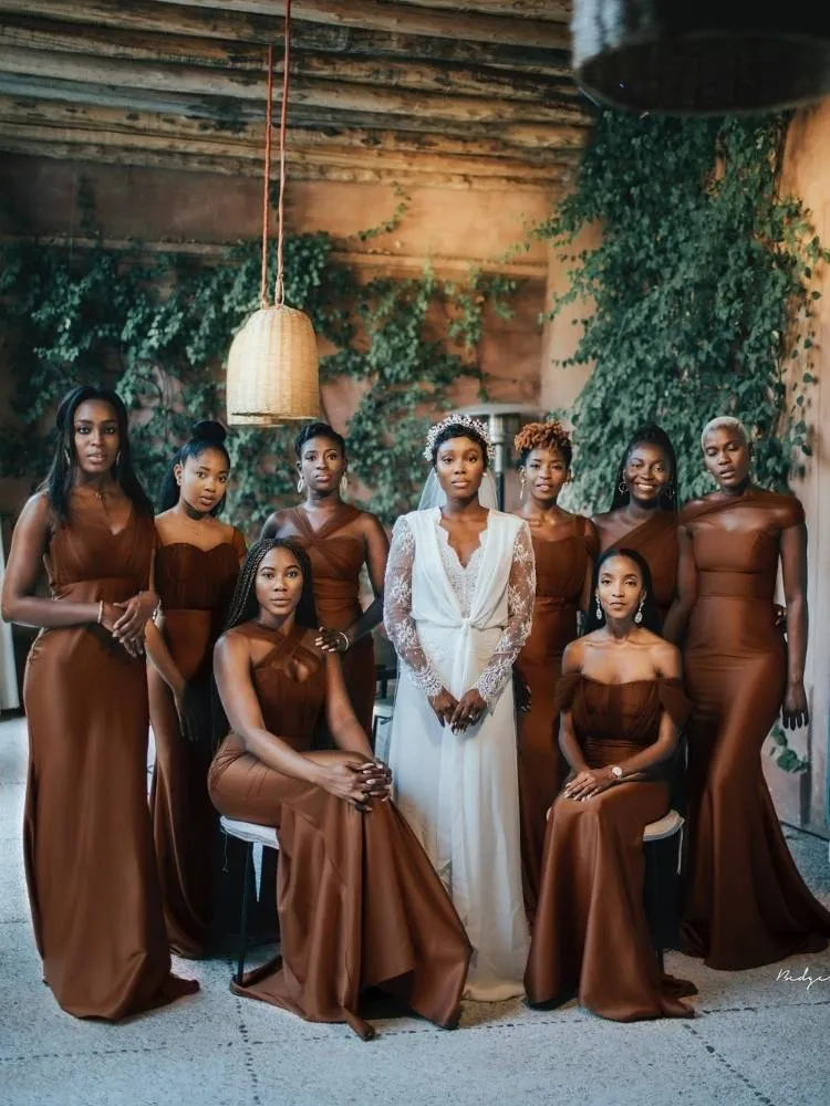Mulheres de pele negra com noiva de branco ao centro e madrinhas de marrom