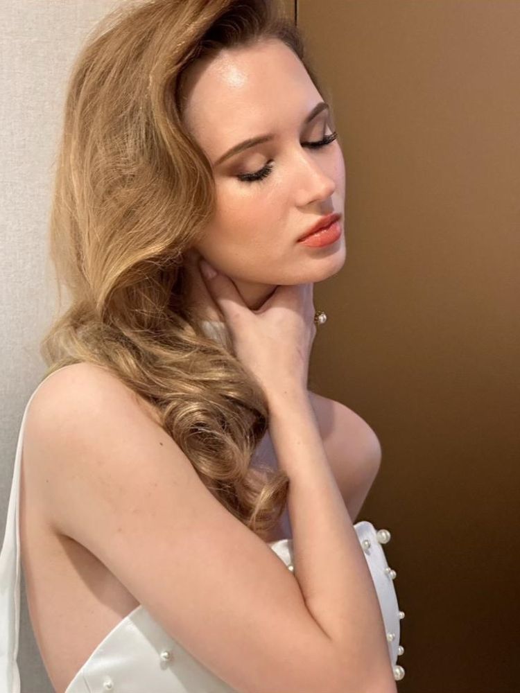 Mulher loira de pele clara usando vestido de noiva e maquiagem natural, com lábios rosados