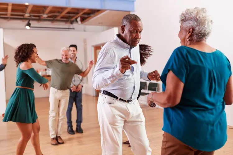 Grupo de pessoas idosas e alguns mais jovens fazendo aula de dança em salão