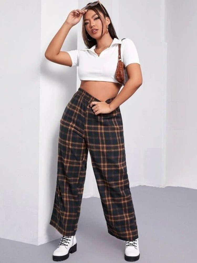 Mulher de pele morena usando cropped branco e calça xadres verde escura