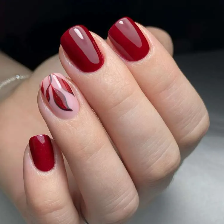 Nail art com vermelho escuro e desenho de folhas no anelar 