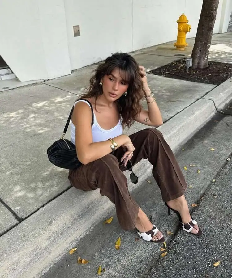 Influencer usando regata branca, calça marrom e mule de vaquinha, minissaia cáqui e sandália plataforma, uma das tendências de sandálias para o verão 2026
