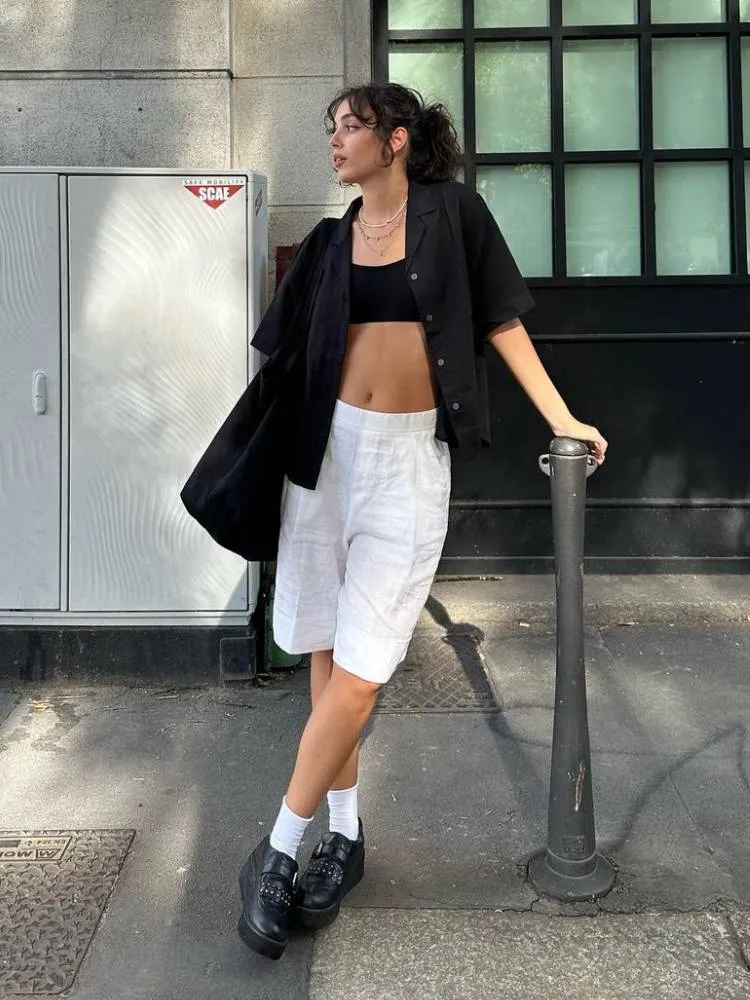 mulher usando top e camisa pretos com bermuda branca 