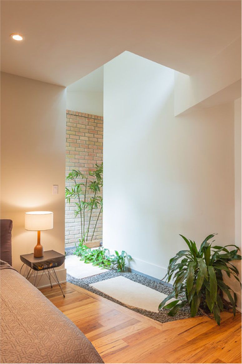 Quarto com mesa de cabeceira, abajur e jardim de inverno com poucas plantas