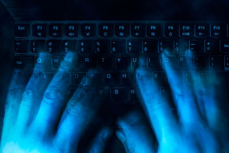 Mãos digitando em notebook aplicando golpe por inteligência artificial