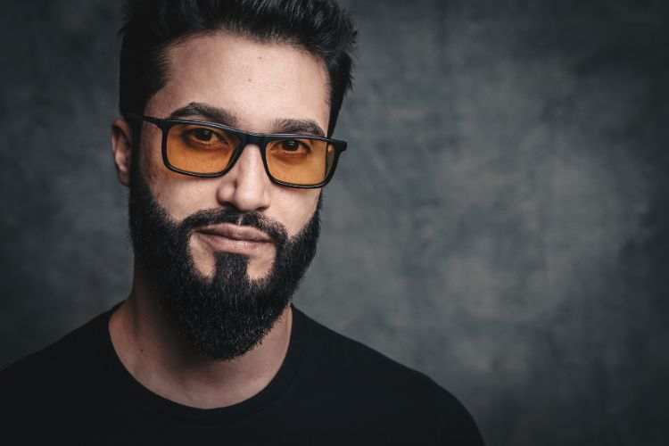 Alan Nicolas, homem de pele clara e barba, usando blusa preta e óculos de sol com lente amarelada