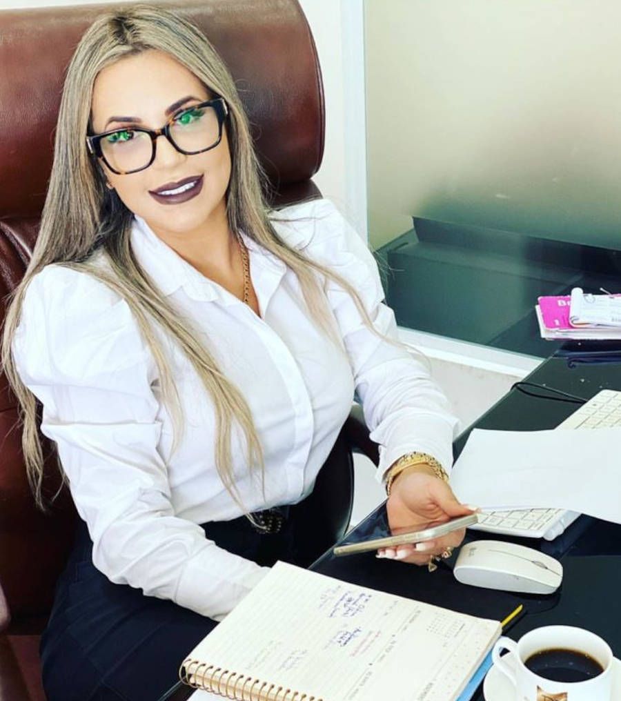 Doutora Deolane vestida de roupa social, com óculos e batom marrom enquanto estuda um processo
